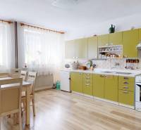 A kitchen in a family house with wooden floors, a green kitchen unit, and a table with chairs.