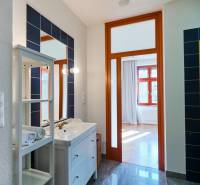 Bathroom entrance with a sink, drawers, mirror, and a view of the sunny room in a 4-room apartment.