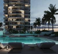 A pool by a lit 3-room apartment in Calpe surrounded by palm trees in the evening.