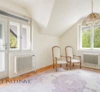 A room in a family house with two chairs, a carpet, two windows, radiators.