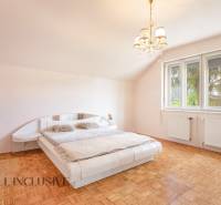 Bright bedroom with a large bed, wooden floor, and chandelier in a family house.