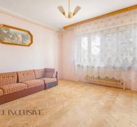 A bright room with a sofa in a family house, sheer curtains, and wooden flooring.