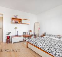Bedroom in a family house with a double bed, shelves, and an armchair, light-colored walls.