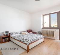 A bright bedroom with a large window, a bed, and a chair in a family house.