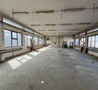 An empty warehouse interior with windows, gray flooring, and hanging lights.