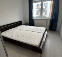 Bedroom in a 2-room apartment with a double bed and a window, blue curtains.