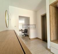 A hallway in a family house with wooden furniture, a mirror, and tiles leads to the living area.