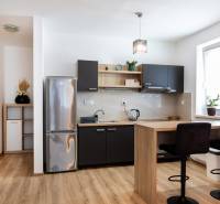 A kitchen in a 2-room apartment with a wooden floor, a bar counter, and a refrigerator.