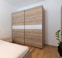 A bedroom with a wooden wardrobe and bed in a 2-room apartment, complemented by a green plant.