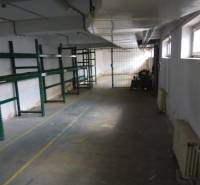 Empty manufacturing space with green metal shelves and windows on one side.
