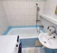 A bathroom in a 3-room apartment with a bathtub and a washing machine, tiled with light tiles.