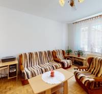 Living room in a three-room apartment with furniture, a table, armchairs, and large windows.