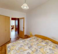 A bedroom in a three-room apartment with a bed, a wooden wardrobe, and open doors to the hallway.