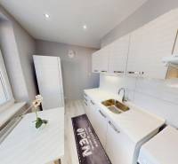 A kitchen in a 2-room apartment with white cabinets and a kitchen mat.