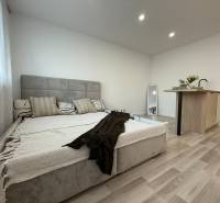 A studio apartment with a bed, kitchen island, and decorative pillows in an open space.