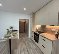 A kitchen in a studio apartment with wooden flooring, white cabinets, and a dining table.