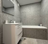 Bathroom with a bathtub and a sink in a studio apartment, with tiles and a mirror.