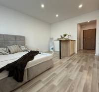 A bed with a wooden floor and a kitchen counter in a studio apartment.