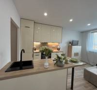 Kitchen of a one-room apartment with a dining counter and a sofa, illuminated by lights.