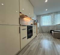 A kitchen in a studio apartment with wooden flooring and built-in appliances.