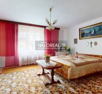 A bedroom in a family house with red curtains, a double bed, and decorative paintings.
