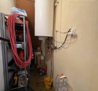 A storage room in the cottage with a boiler, shelves, and bottles offers practical storage space.