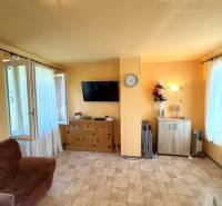 A bright room in a cottage with a brown couch and a cabinet, windows with white curtains.