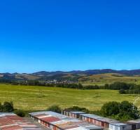 A landscape with green fields, hills, and a parking lot on Okružná in Stará Ľubovňa.