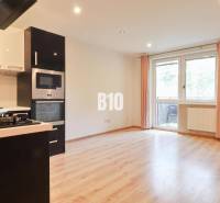 A kitchen in a 3-room apartment with a light wooden floor design and built-in appliances.