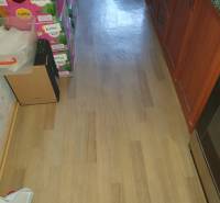 The floor in the kitchen of a 2-room apartment with boxes in a pile, wooden cabinets on the right.