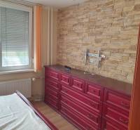 Bedroom in a 2-room apartment with stone wallpaper and wooden dressers.