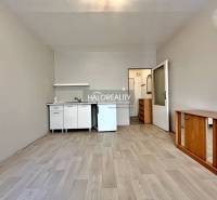 Studio apartment with a white kitchen unit, wooden furniture, and laminate flooring.