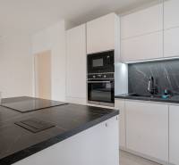 A kitchen in a 3-room apartment with white cabinets, a black countertop, and an orchid.