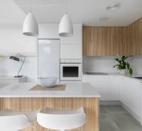 A kitchen in a villa with white and wooden cabinets, illuminated by modern lamps.