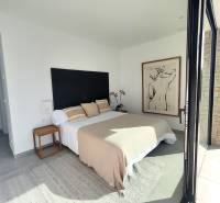 A bright bedroom in a villa with a bed, a painting on the wall, and a view outside.