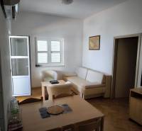 A clear one-room apartment with wooden flooring, a table, a television, and a sofa.