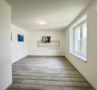 A spacious room with wooden flooring, white walls, and a large window in a family house.