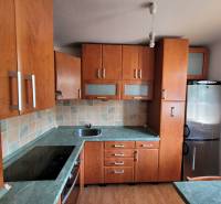 A kitchen in a studio apartment with wooden cabinets, a stainless steel sink, and an electric stove.