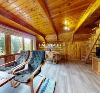 Wooden interior of a cabin with armchairs, a table, and a staircase in a mountain setting.