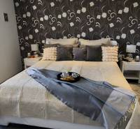 A bedroom in a family house with floral wallpaper and a bed decorated with pillows.
