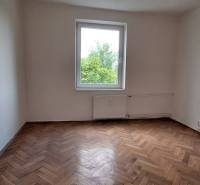 An empty room in a 3-room apartment with a parquet floor and a window overlooking greenery.