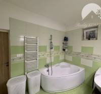 A bathroom in a family house with a corner bathtub and green tiles.