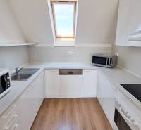 A kitchen in a 4-room apartment with wooden flooring, white furniture, and a skylight.