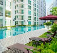 Pattaya, construction of apartments with a swimming pool, deck chairs, and umbrellas in a residential area.