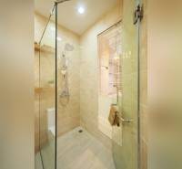 Bathroom in a 2-room apartment with a glass shower enclosure and light-colored tiles.