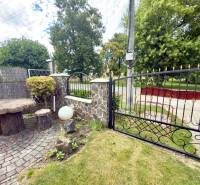 A family house in Koválov with a wrought iron gate, a stone table, and greenery.