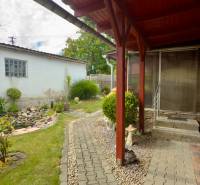 The courtyard of a family house in Koválov with a covered terrace, landscaped greenery, and a walkway.