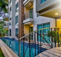 A swimming pool and the facade of a residential building in Pattaya surrounded by greenery.