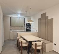 Dining room in a holiday apartment with a kitchen, light chairs, and gray panels on the wall.