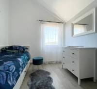 A bedroom in a holiday apartment with a bed, white dresser, and chair on a wooden floor.